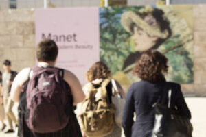 3 people walking towards a sign that says Manet and has an image of a woman with a bonnet and an umbrella.