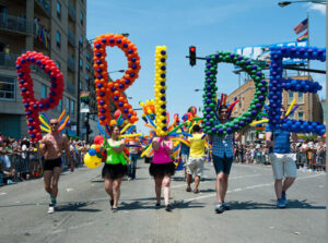 People marching in a pride parade with balloons gathered in the shapes of the letters p r i d e