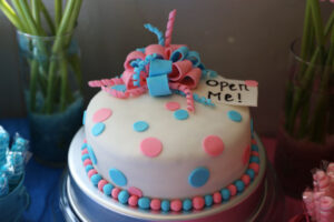 Cake with pink and blue decorations and a tag that says, "Open me!"