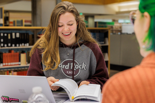 A student smiles while reading a book in the library