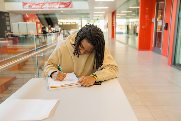 An EWU student sits at a table writing in a notebook