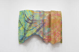 A close-up of two overlapping, brightly colored woven textiles. The left piece features turquoise, yellow, green, and dark curved lines, while the right piece combines coral pink, orange, and muted green.