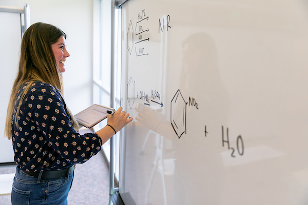 A student writes a chemistry equation on a white board