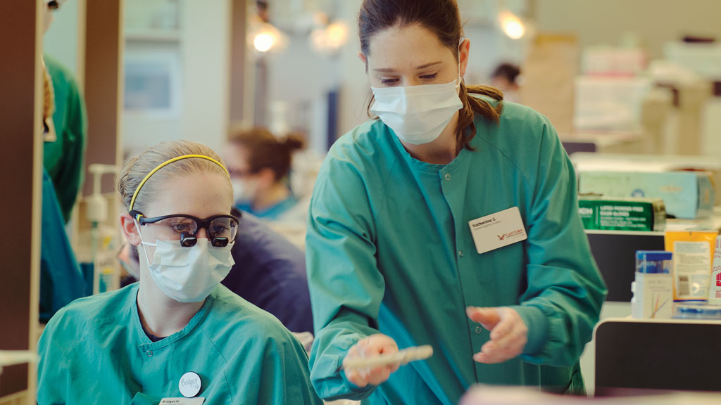 Two dental hygiene students work in the lab wearing full gear