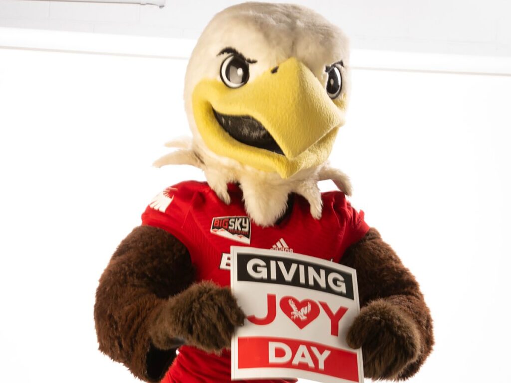 Swoop holding a sign that says "Giving Joy Day."