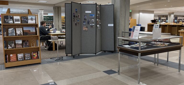 photo of the Veterans Day display in the lobby of JFK Library. Display includes recent books, a wall to offer remembrances, and two display cases of graphic novels from the Global War on Terror era.