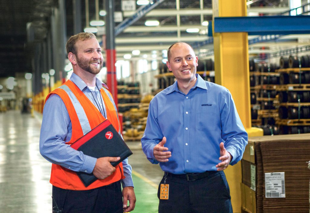 Photo: Two men on a factory floor. One has an Eagle-branded folder