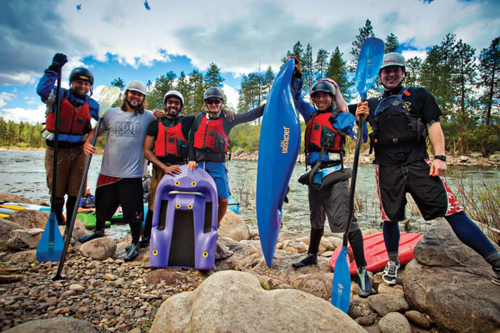 Photo of six EWU students posing with water sports gear on the shore of a river.