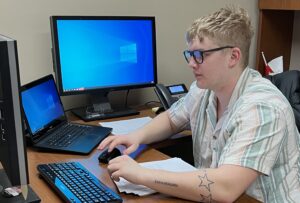 Sam, pictured working on a computer in the university's Advancement department, is doing research and storytelling that supports student success.