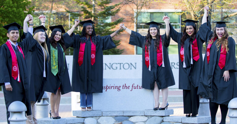 Photo of studnents in caps and gowns holding hands with their arms up high.