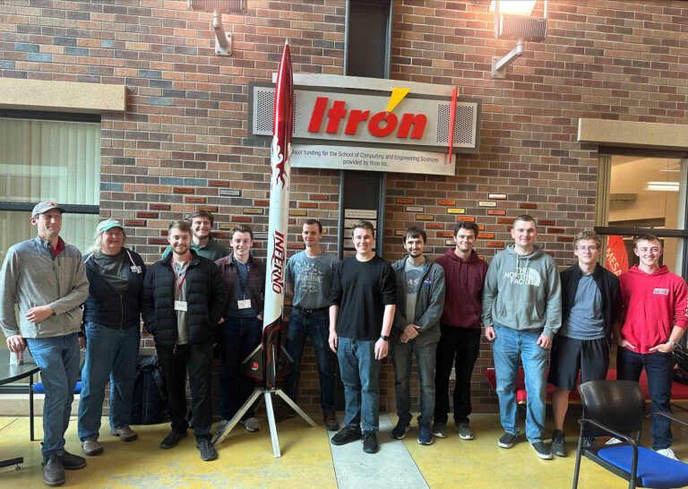 Photo of the members of the aerospace club with an Itron sponsorship sign in the background.