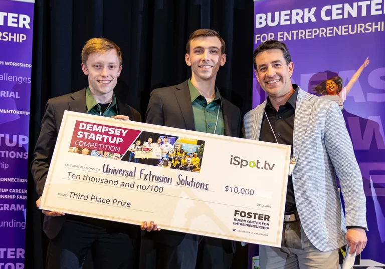 Photo of three team members holding up a big fake check that symbolizes their prize award.