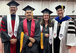 Two cybersecurity students in caps and gowns along with two gowned faculty members.