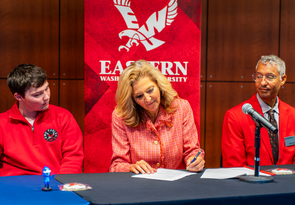 President Shari McMahan signs agreement as student and provost look on. 
