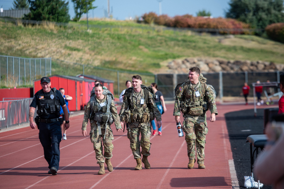 Officer Greg Karlis on the track with three ROTC students carrying backpacks.
