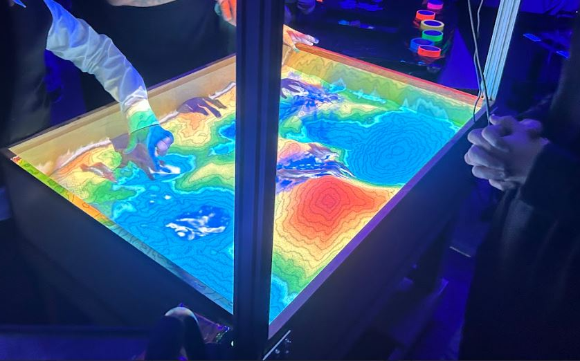 Lighted topographical map with kids' hands touching it.