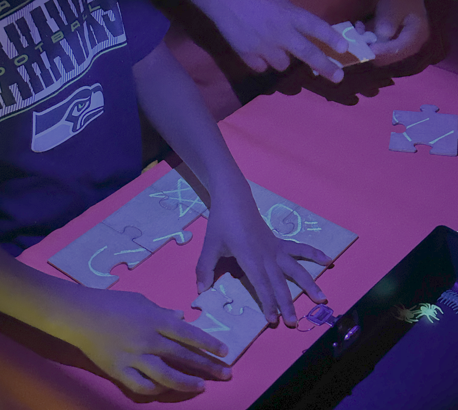 Students working with puzzle pieces under purple florescent light.