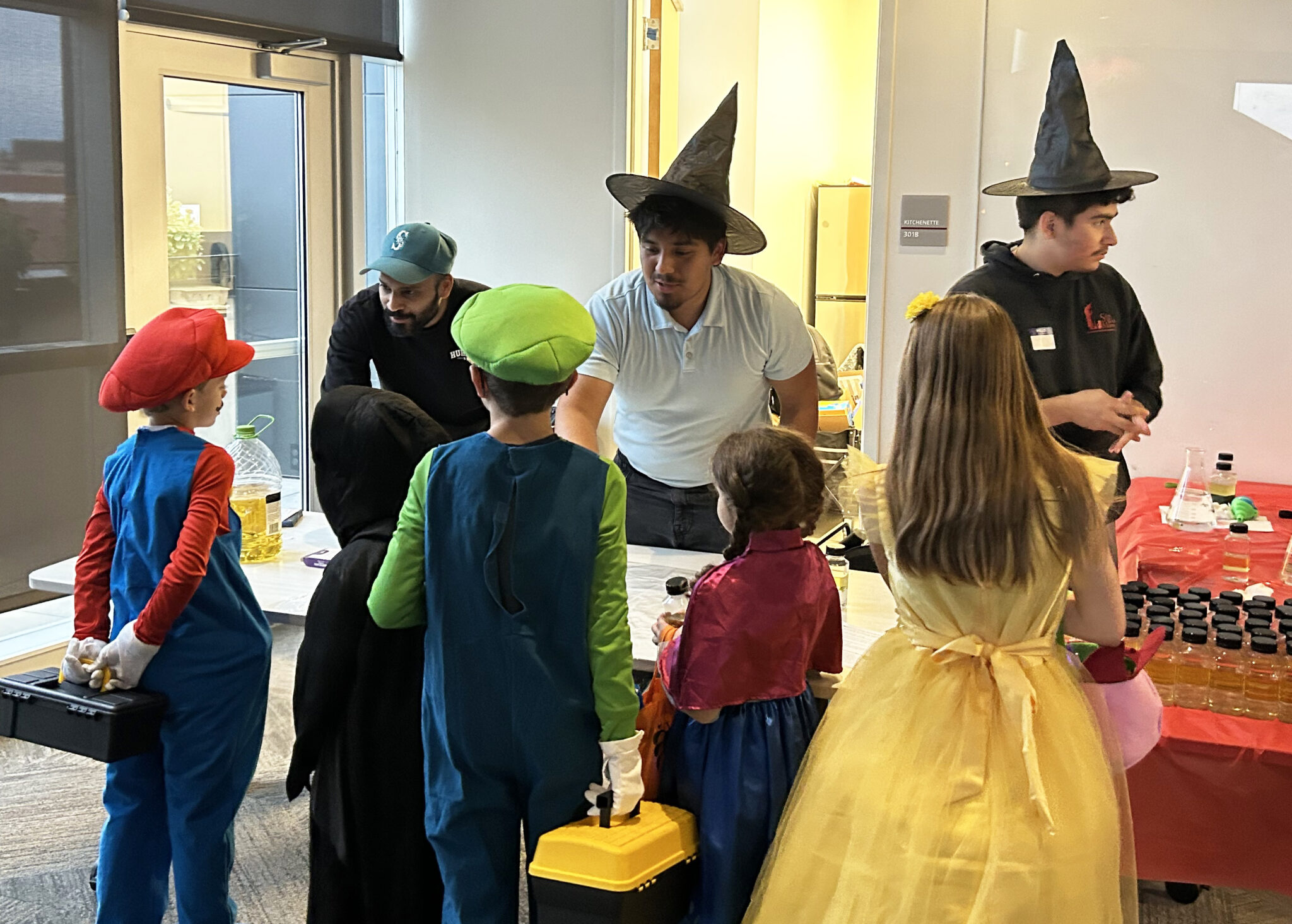 Students wearing witch hats working with children in costumes.