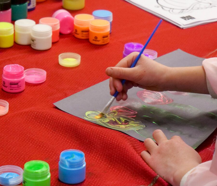 Arm painting on a table with paints nearby.