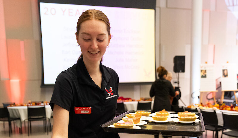 Catering employee smiles while restocking slices of pie.