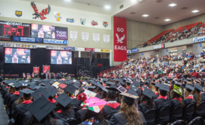 Commencement photo taken behind the rows of grads in caps and gowns looking at the speaker.