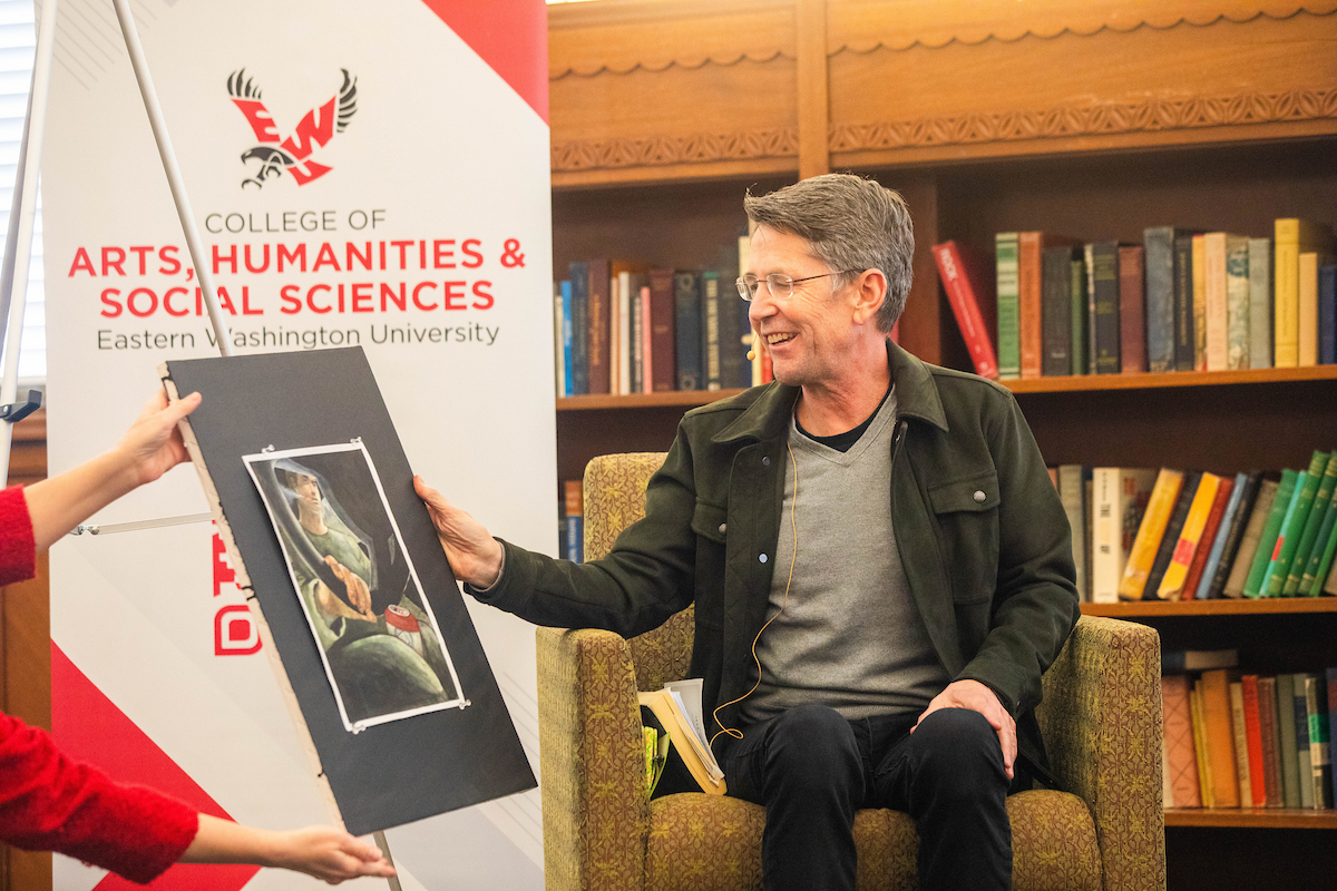 Jess Walter smiling while looking at a painting a student made to illustrate one of his stories.