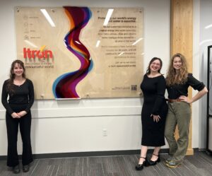 Three design students with an Itron-branded sign they designed in partnership with Itron.