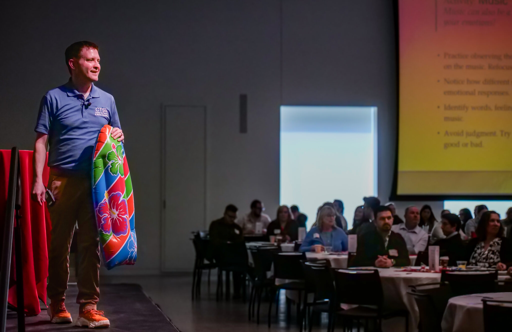 Presenter holding an inflatable surfboard and addressing the crowd.