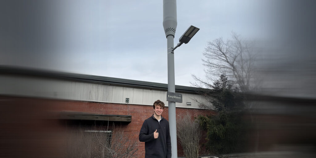 man stands beside telecommunications pole and industrial building.