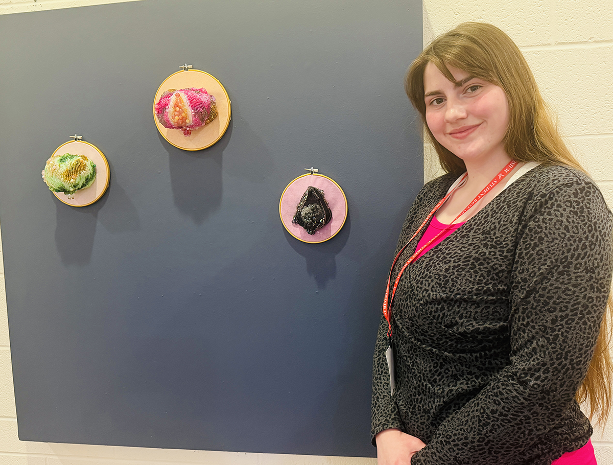 Student stands near three piece art made of beads and felt.