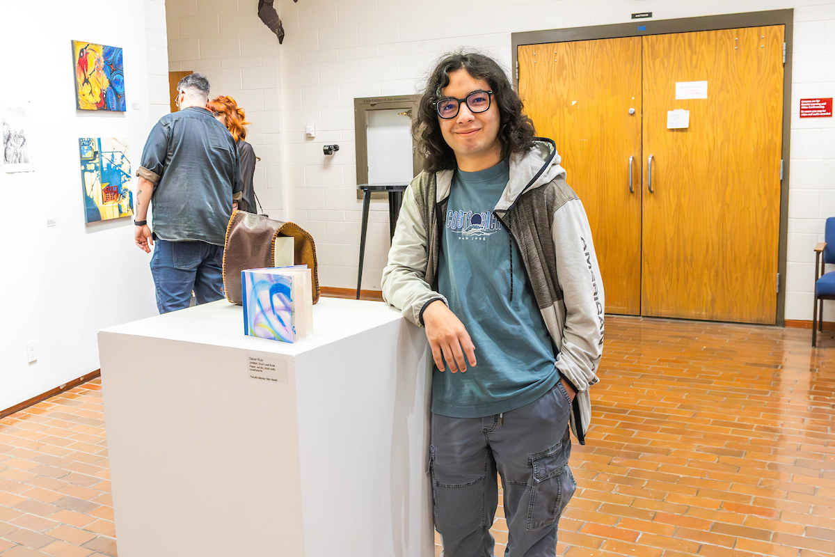 Student leans on display, next to the book he created