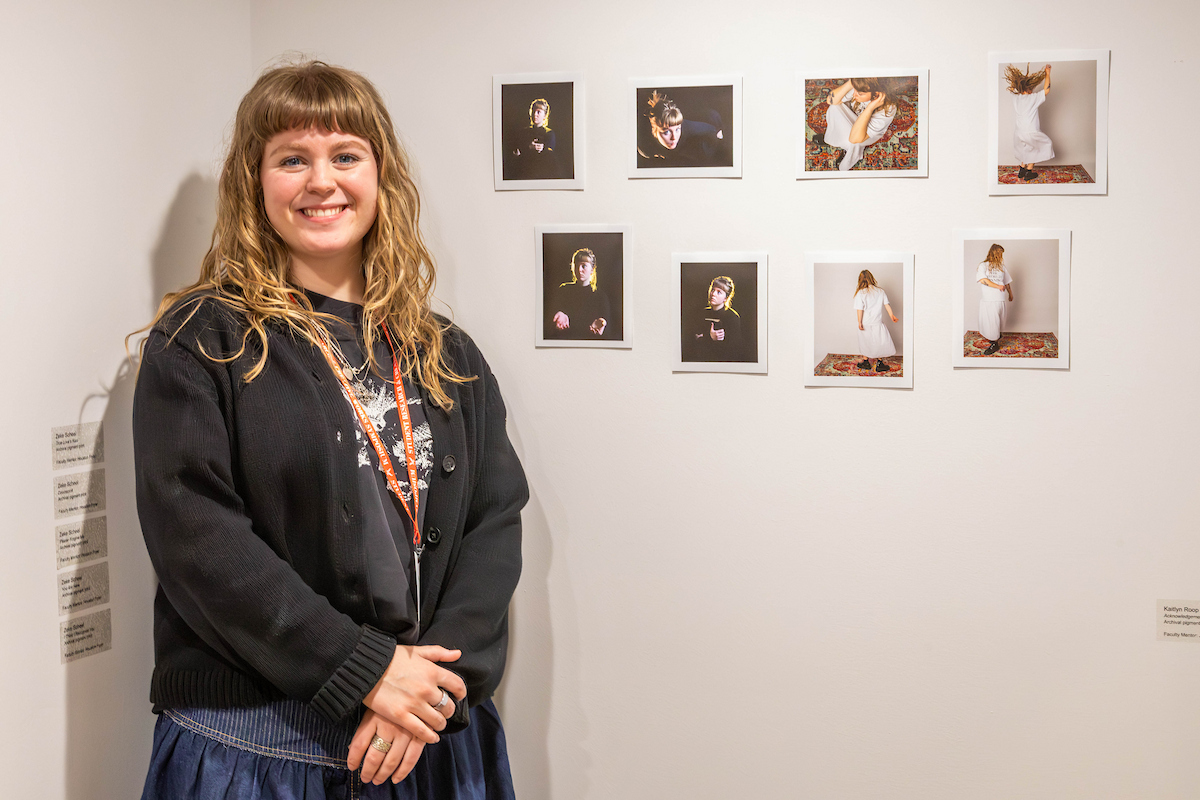 Student stands in front of eight posted photos that she created.