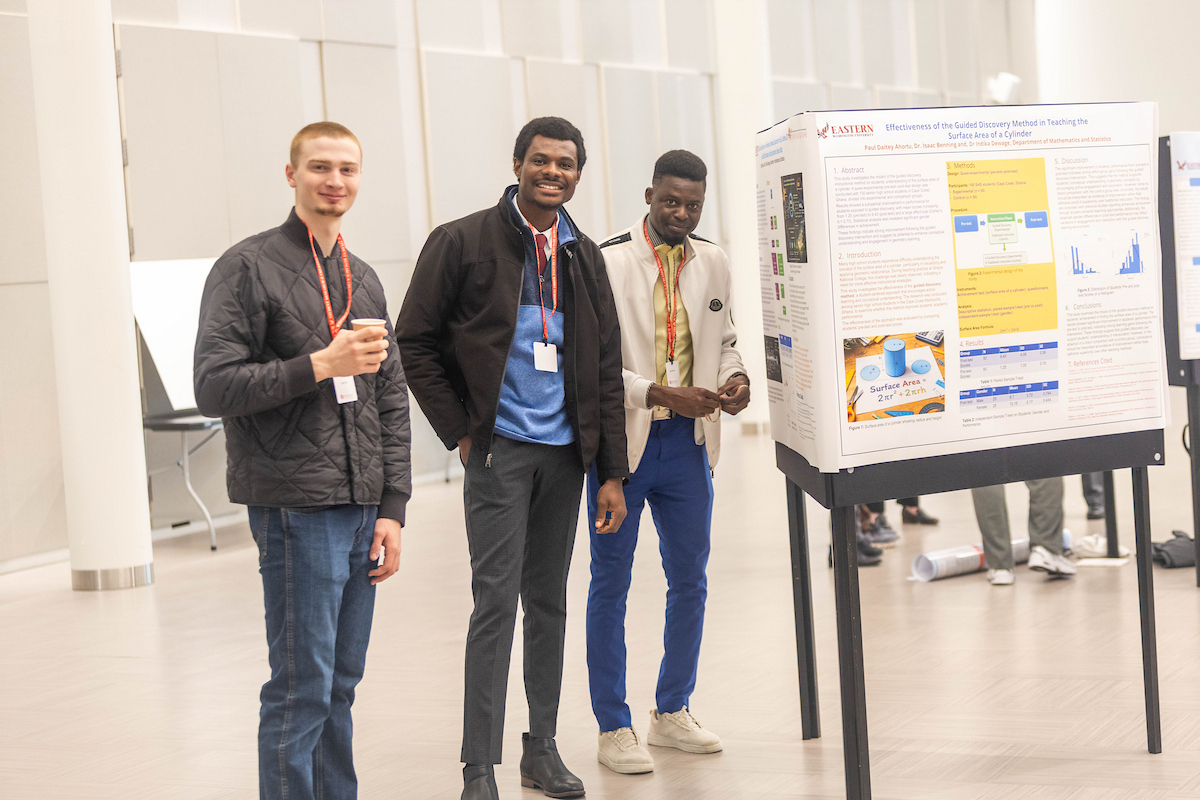 Three students standing by their poster presentation