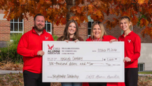 Haleigh Camberg holds a big check with the Alumni Association's Riley Baxter, Sarah Boldizar and Kelsey Hatch-Brecek.